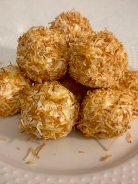 A small stack of coconut fat bombs rolled in toasted shredded coconut, creamy bite-sized keto snacks stacked on a white plate.