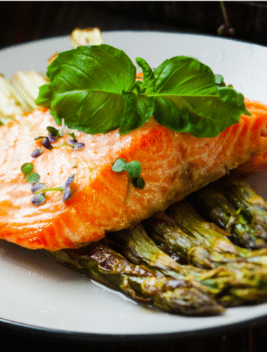 Salmon piled on top of asparagus on a white plate.